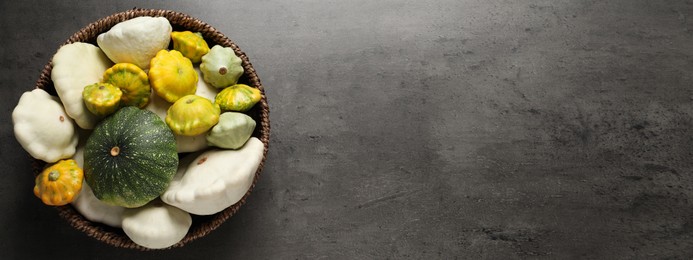 Fresh ripe pattypan squashes in wicker bowl on grey table, top view with space for text. Banner design