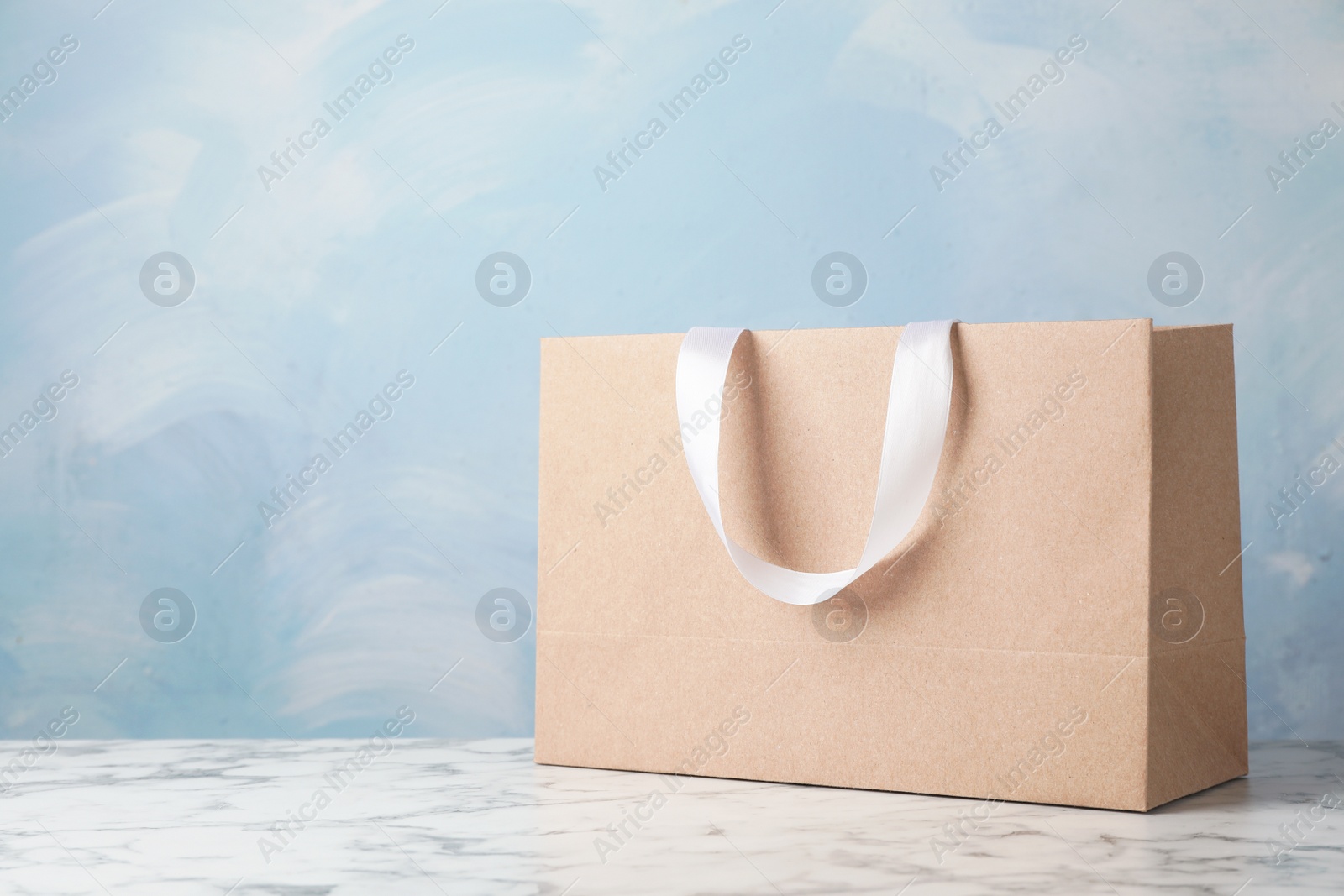 Photo of Paper shopping bag with ribbon handles on table against color background. Mockup for design