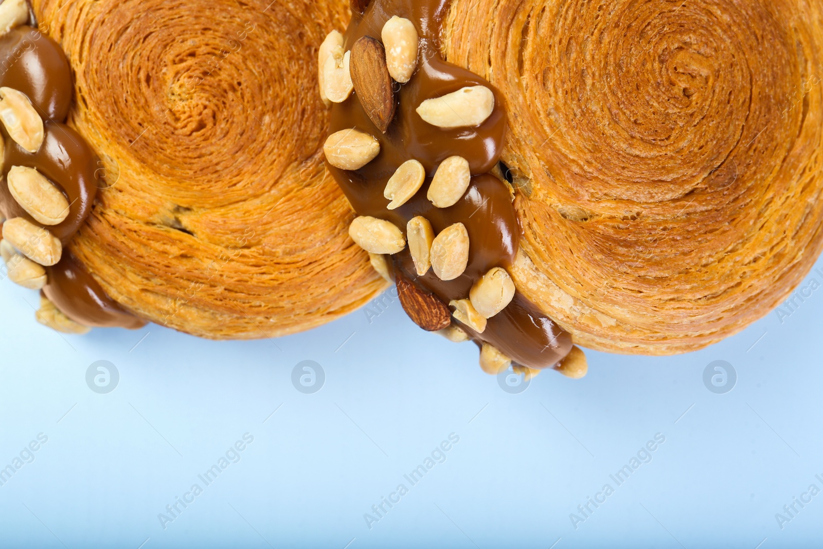 Photo of Tasty puff pastry. Supreme croissants with chocolate paste and nuts on light blue background, top view. Space for text
