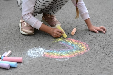 Photo of Little child drawing rainbow with chalk on asphalt, closeup