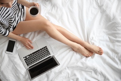 Female blogger with laptop and cup of coffee on bed, top view