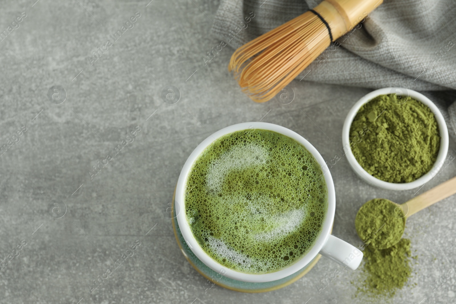 Photo of Cup of fresh matcha latte, powder and bamboo whisk on grey table, flat lay. Space for text