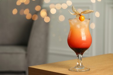 Refreshing cocktail decorated with physalis fruit on wooden table indoors. Space for text