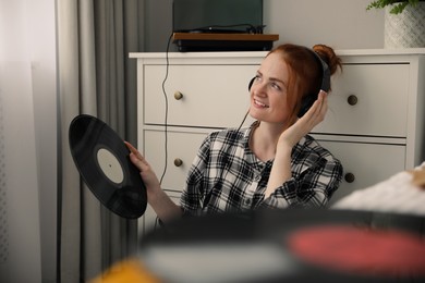 Photo of Young woman listening to music with turntable at home