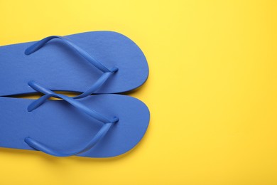 Stylish blue flip flops on yellow background, top view. Space for text