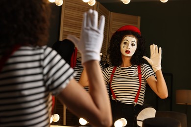 Young woman in mime costume posing near mirror indoors