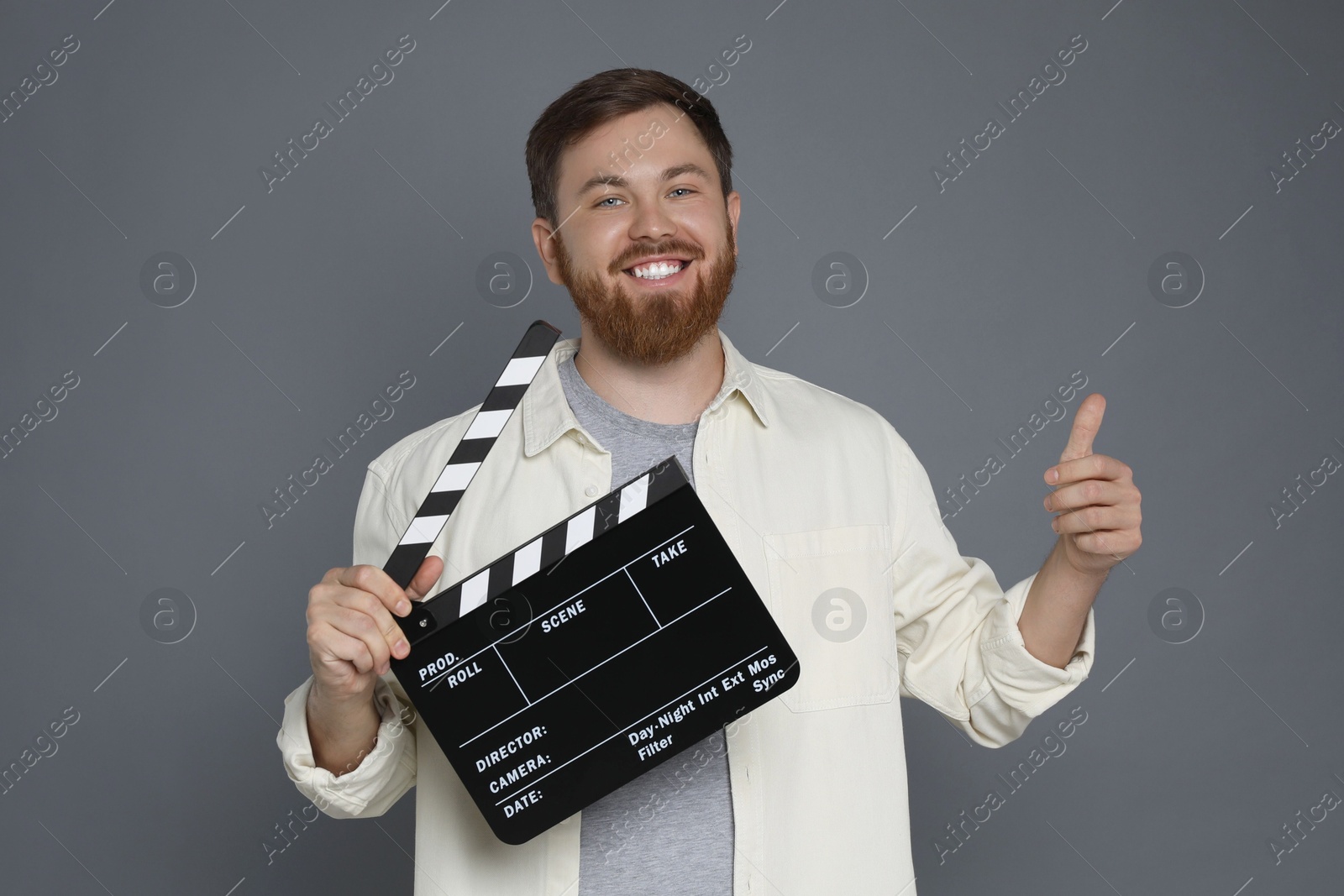 Photo of Making movie. Smiling man with clapperboard showing thumb up on grey background