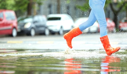 Photo of Woman with red rubber boots running in puddle, closeup. Rainy weather