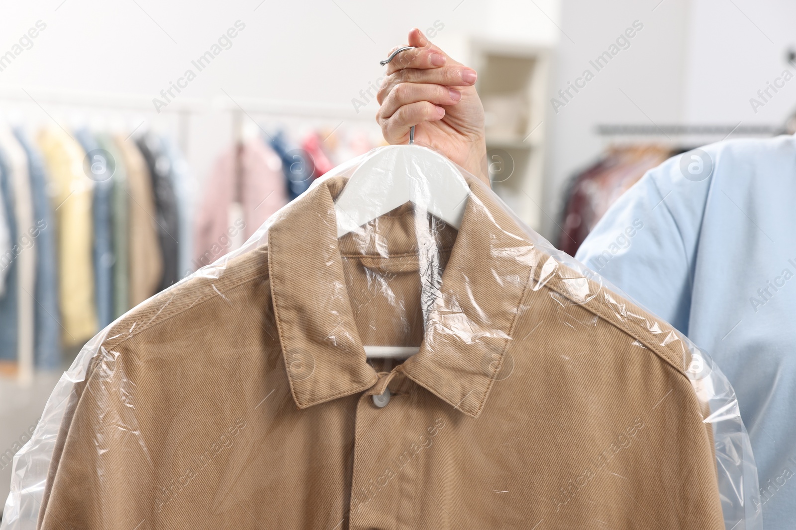 Photo of Dry-cleaning service. Woman holding shirt in plastic bag indoors, closeup