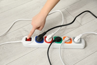 Photo of Woman pressing power button of extension cord on floor, closeup. Electrician's professional equipment