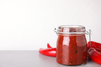 Photo of Glass jar of hot chili sauce with peppers on table against white background. Space for text