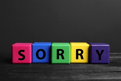 Apology. Word Sorry made of colorful cubes on black wooden table