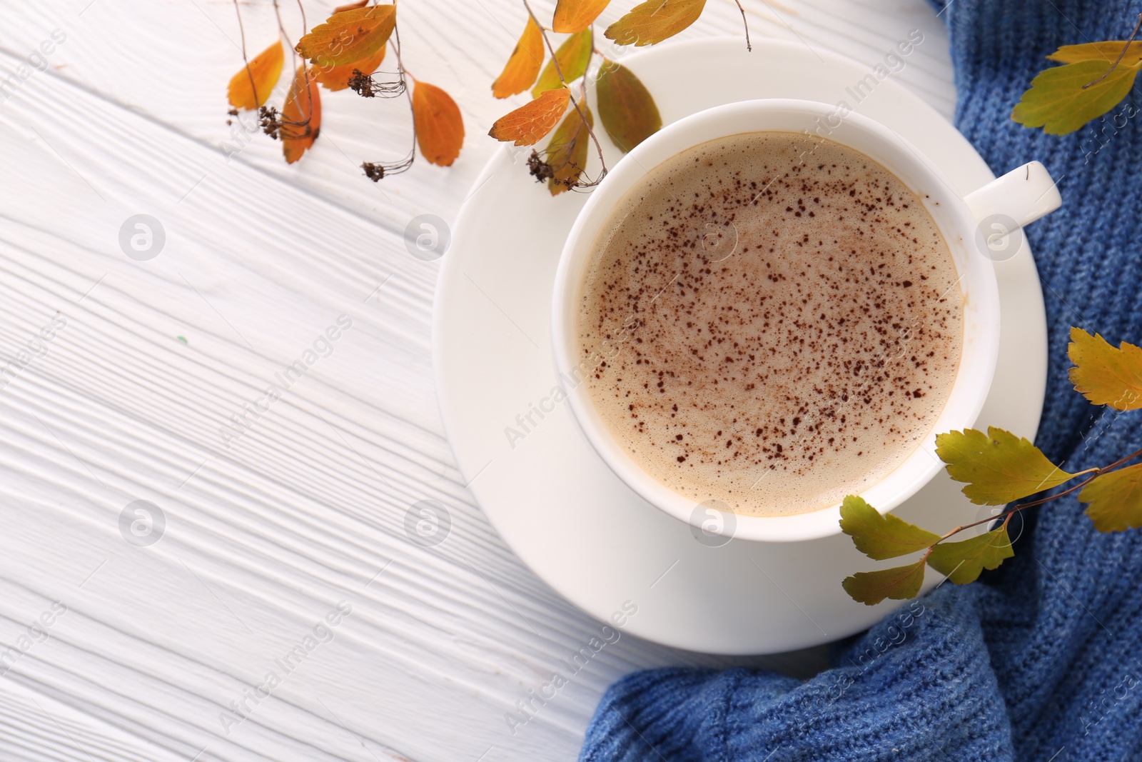 Photo of Cup of hot drink, leaves and knitted sweater on white wooden table, flat lay with space for text. Cozy autumn atmosphere