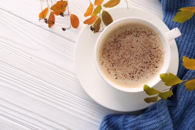 Cup of hot drink, leaves and knitted sweater on white wooden table, flat lay with space for text. Cozy autumn atmosphere