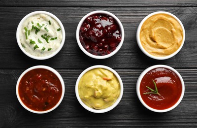 Different tasty sauces in bowls on black wooden table, flat lay