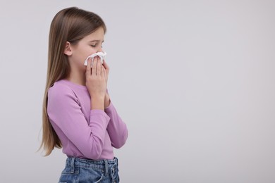 Sick girl with tissue coughing on light background, space for text