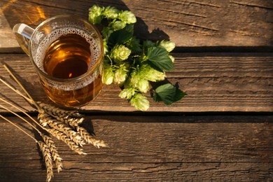 Photo of Mug with beer, fresh hops and ears of wheat on wooden table, above view. Space for text