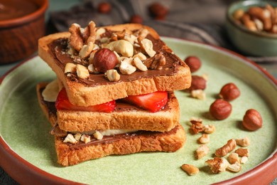 Photo of Tasty toasts with chocolate spread, nuts, strawberries and banana served on table, closeup