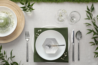 Elegant table setting with green plants on light cloth, flat lay