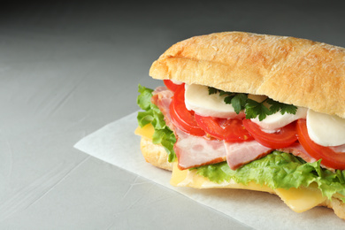 Photo of Delicious sandwich with fresh vegetables and mozzarella on grey table, closeup