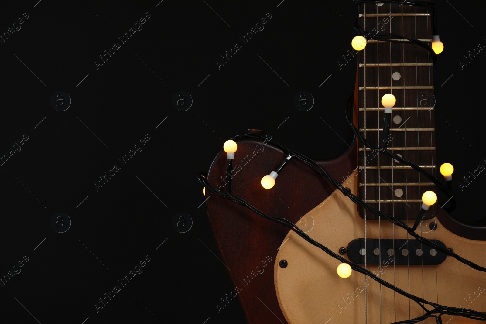 Photo of Guitar with golden lights on black background, space for text. Christmas music