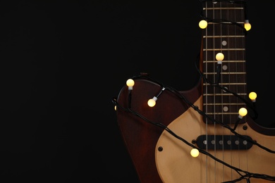 Photo of Guitar with golden lights on black background, space for text. Christmas music