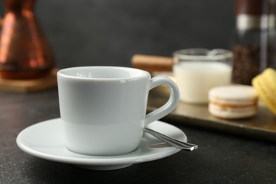 Photo of White espresso cup, spoon and saucer on dark textured table, closeup