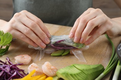 Photo of Woman wrapping spring roll at table with products, closeup