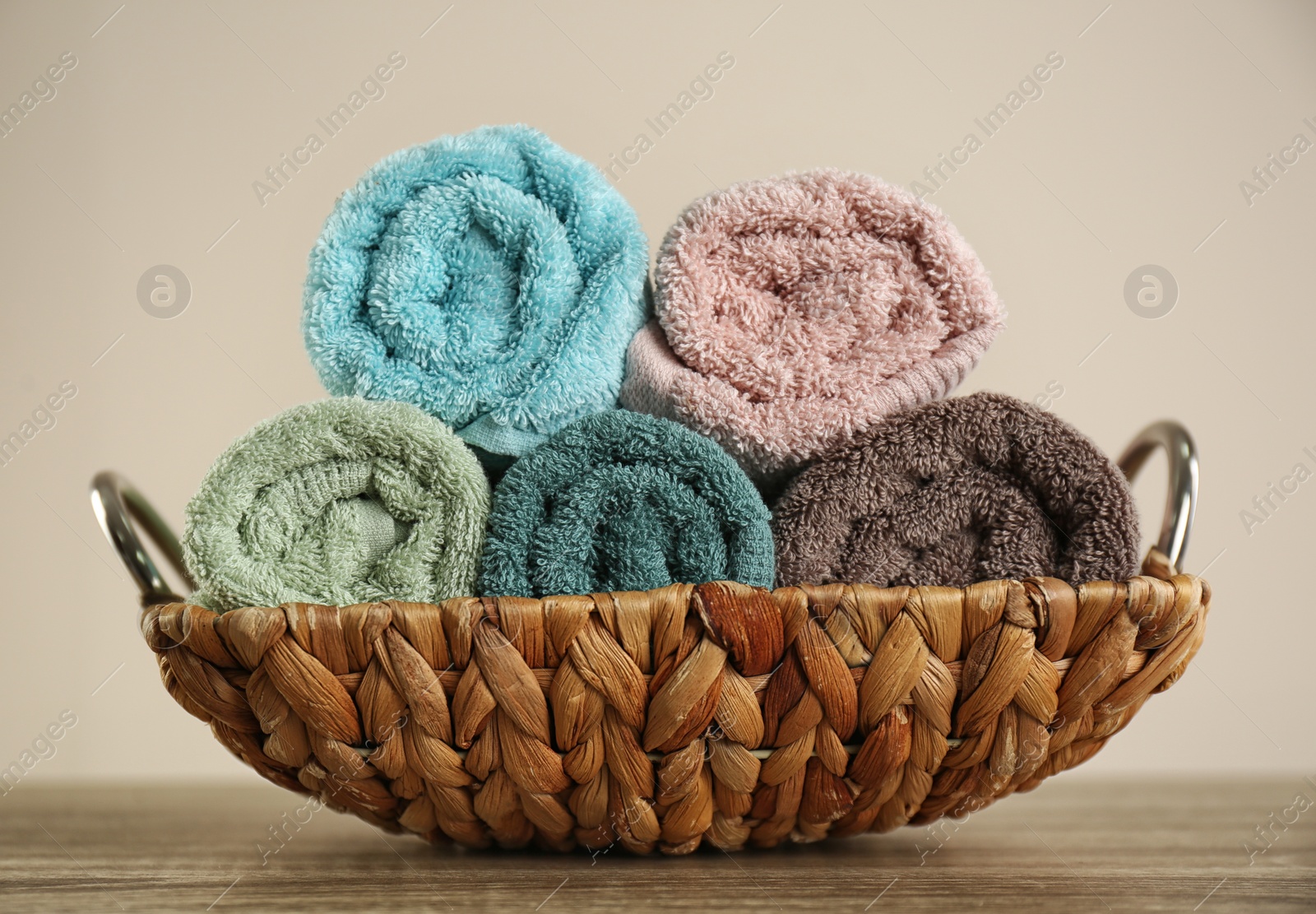 Photo of Wicker basket with rolled bath towels on wooden table