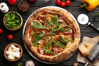 Photo of Tasty pizza with meat and arugula on black wooden table, flat lay