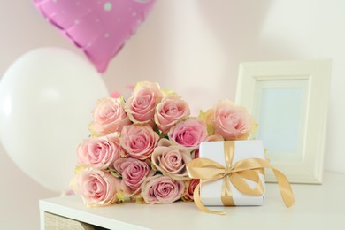 Beautiful bouquet of roses, gift and balloons on white table. Happy birthday greetings