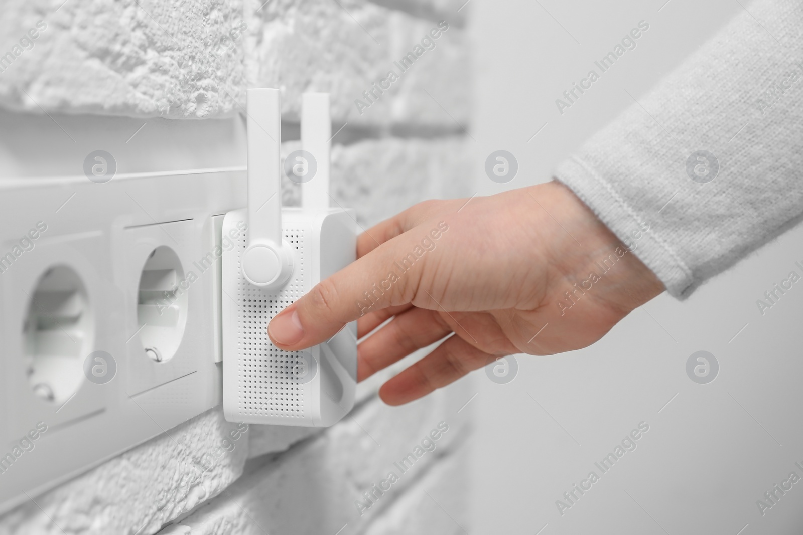 Photo of Woman turning on wireless Wi-Fi repeater indoors, closeup