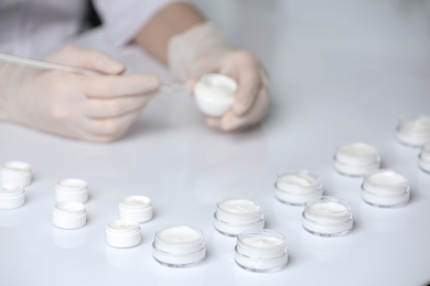 Photo of Scientist working in laboratory, focus on jars with different cosmetic products
