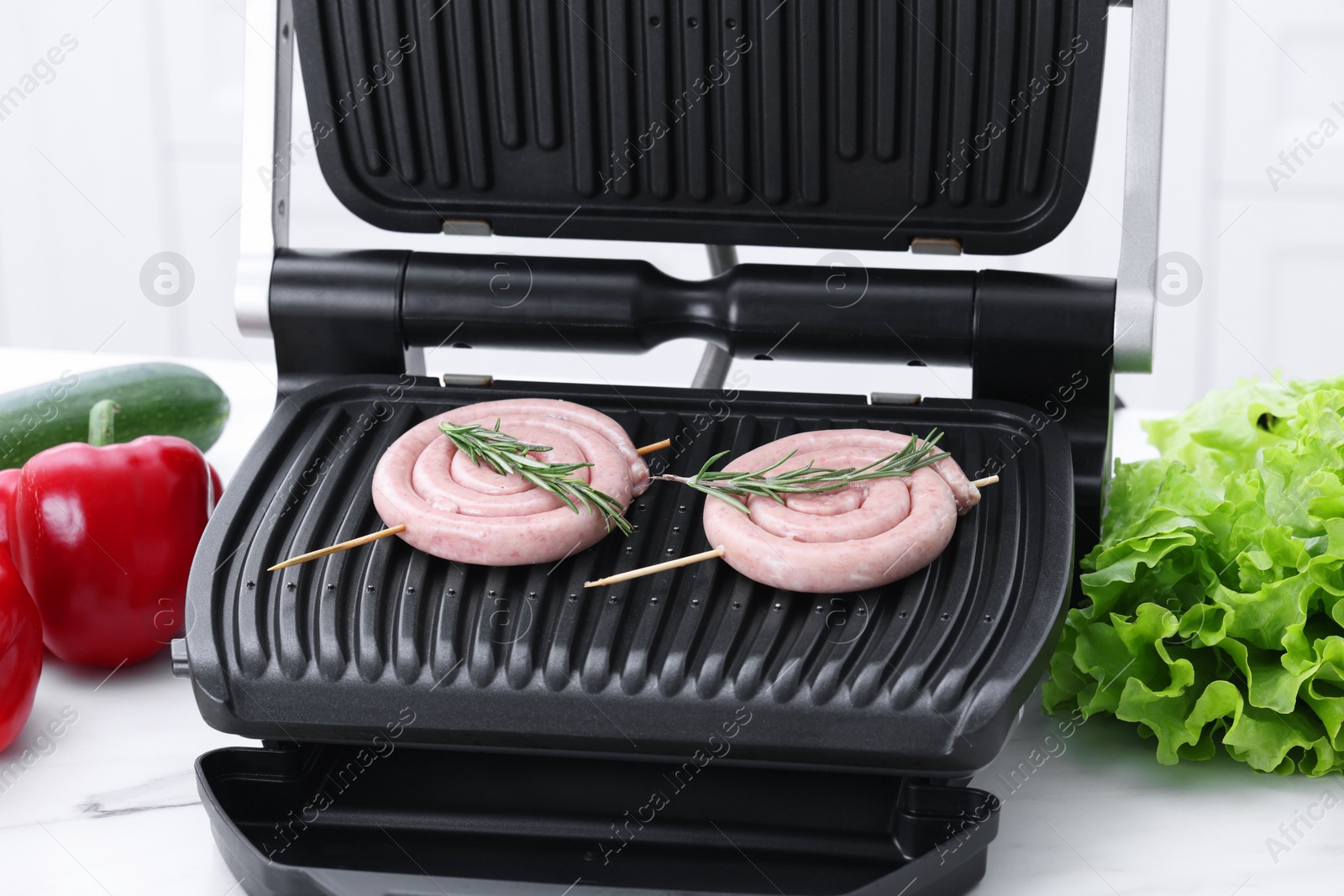 Photo of Electric grill with homemade sausages and rosemary on white table