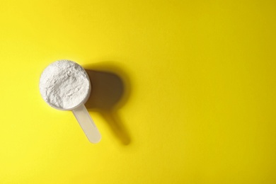 Photo of Scoop of protein powder on yellow background, top view with space for text