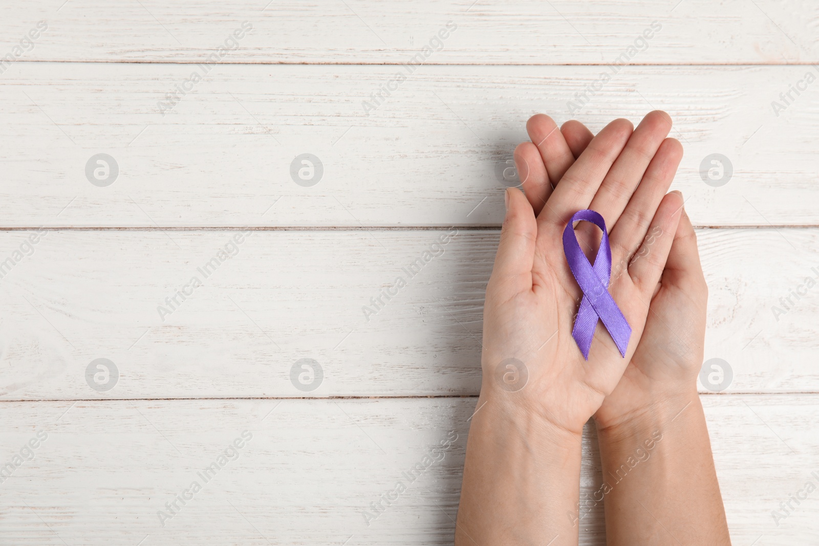 Photo of Woman holding purple ribbon on white wooden background, top view with space for text. Domestic violence awareness