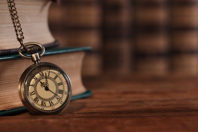 Photo of Pocket clock with chain and books on wooden table, closeup. Space for text