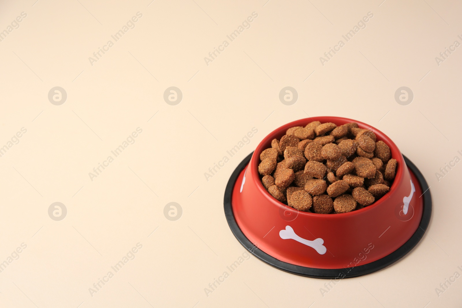 Photo of Dry dog food in feeding bowl on beige background. Space for text