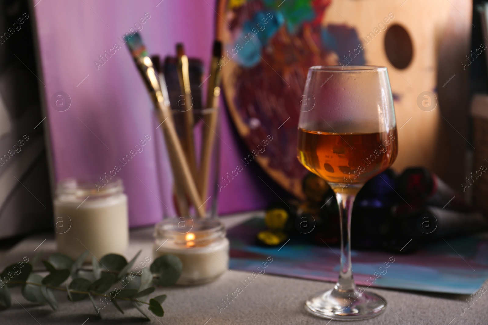 Photo of Glass of wine and brushes with colorful paints on light gray table, space for text