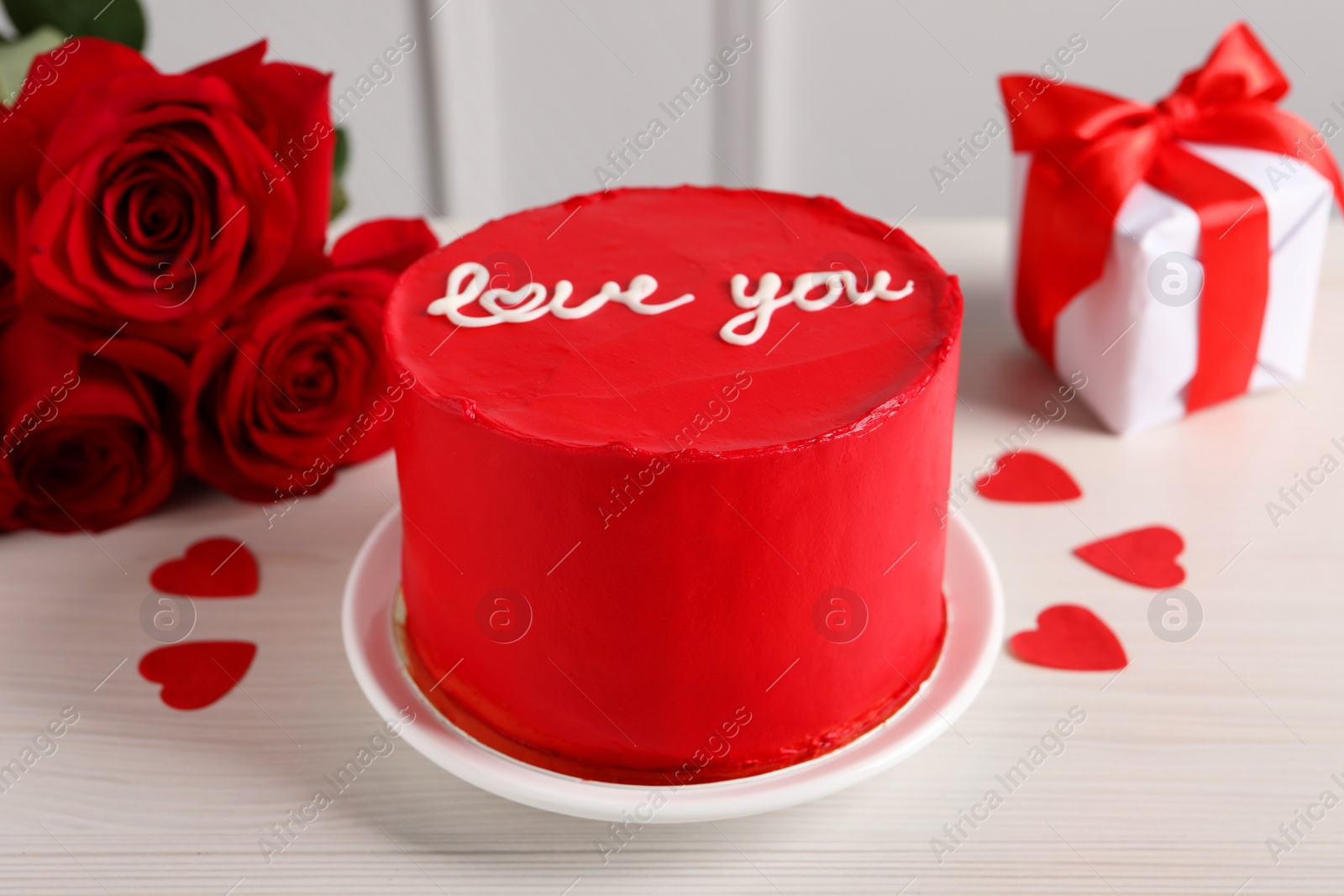 Photo of Bento cake with text Love You, roses, paper hearts and gift box on white wooden table. St. Valentine's day surprise