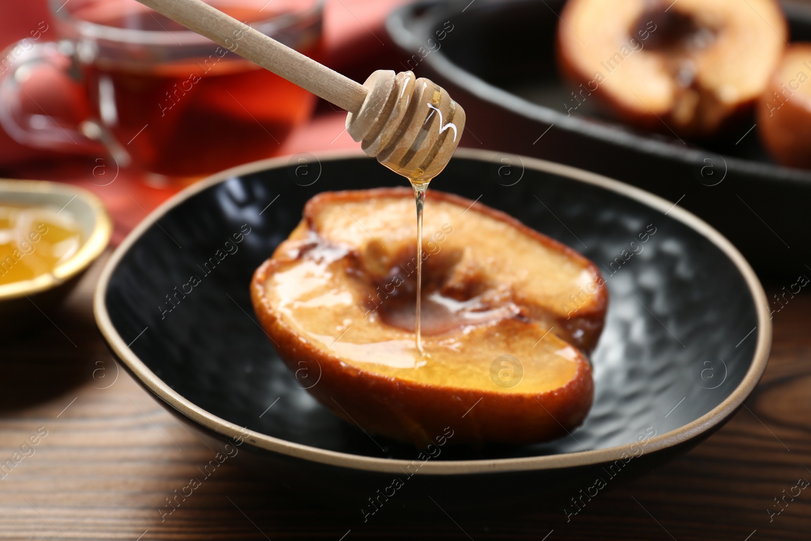 Photo of Pouring honey onto tasty baked quince in bowl at wooden table, closeup