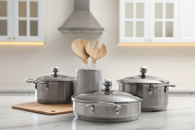 Set of stainless steel cookware and kitchen utensils on white table indoors