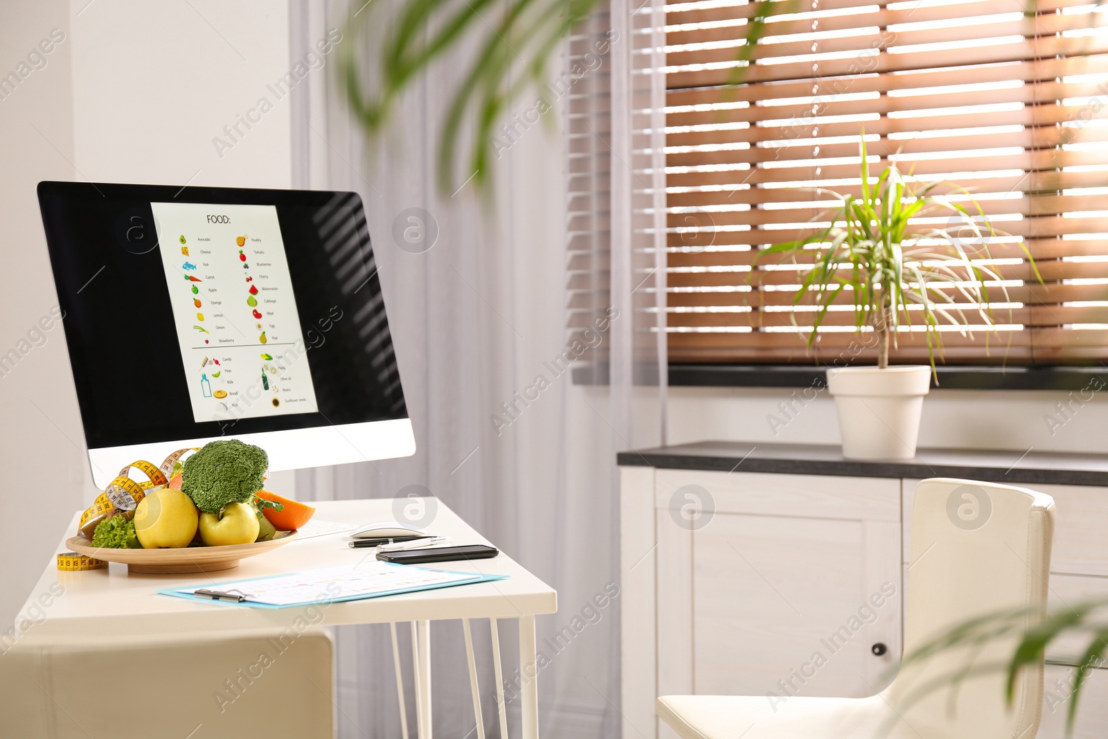 Photo of Measuring tape, vegetables and fruits near computer on desk in nutritionist's office. Space for text