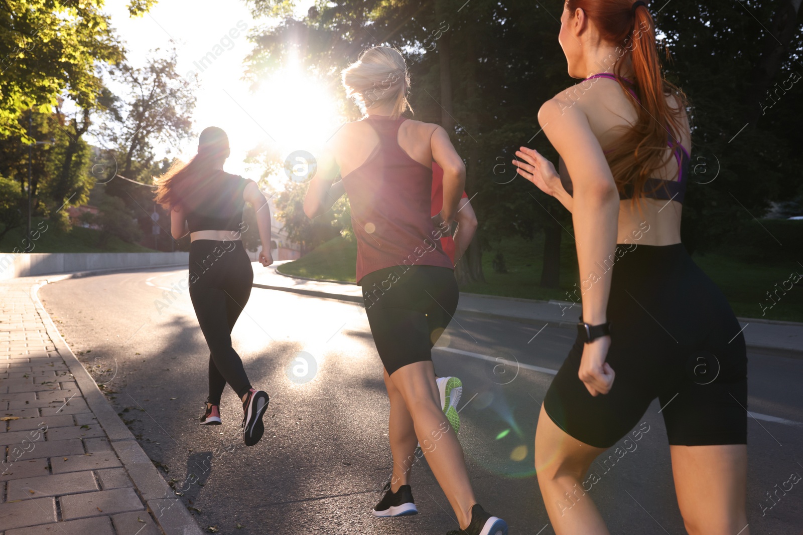 Photo of Group of people running outdoors on sunny day, back view