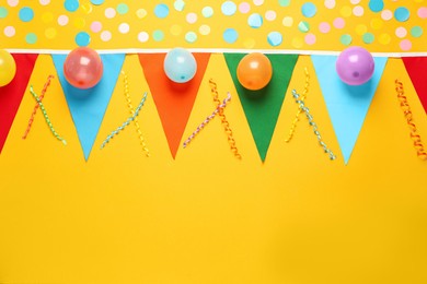 Bunting with colorful triangular flags and other festive decor on yellow background, flat lay. Space for text