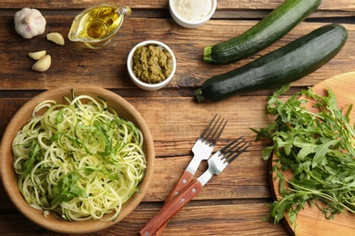 Photo of Tasty zucchini pasta with arugula, sauce and ingredients on wooden table, flat lay