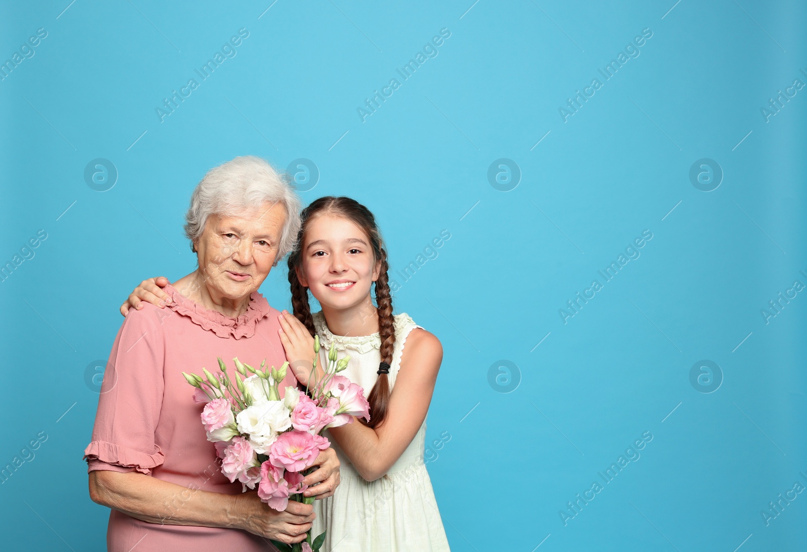Photo of Cute girl and her grandmother with flowers on light blue background. Space for text