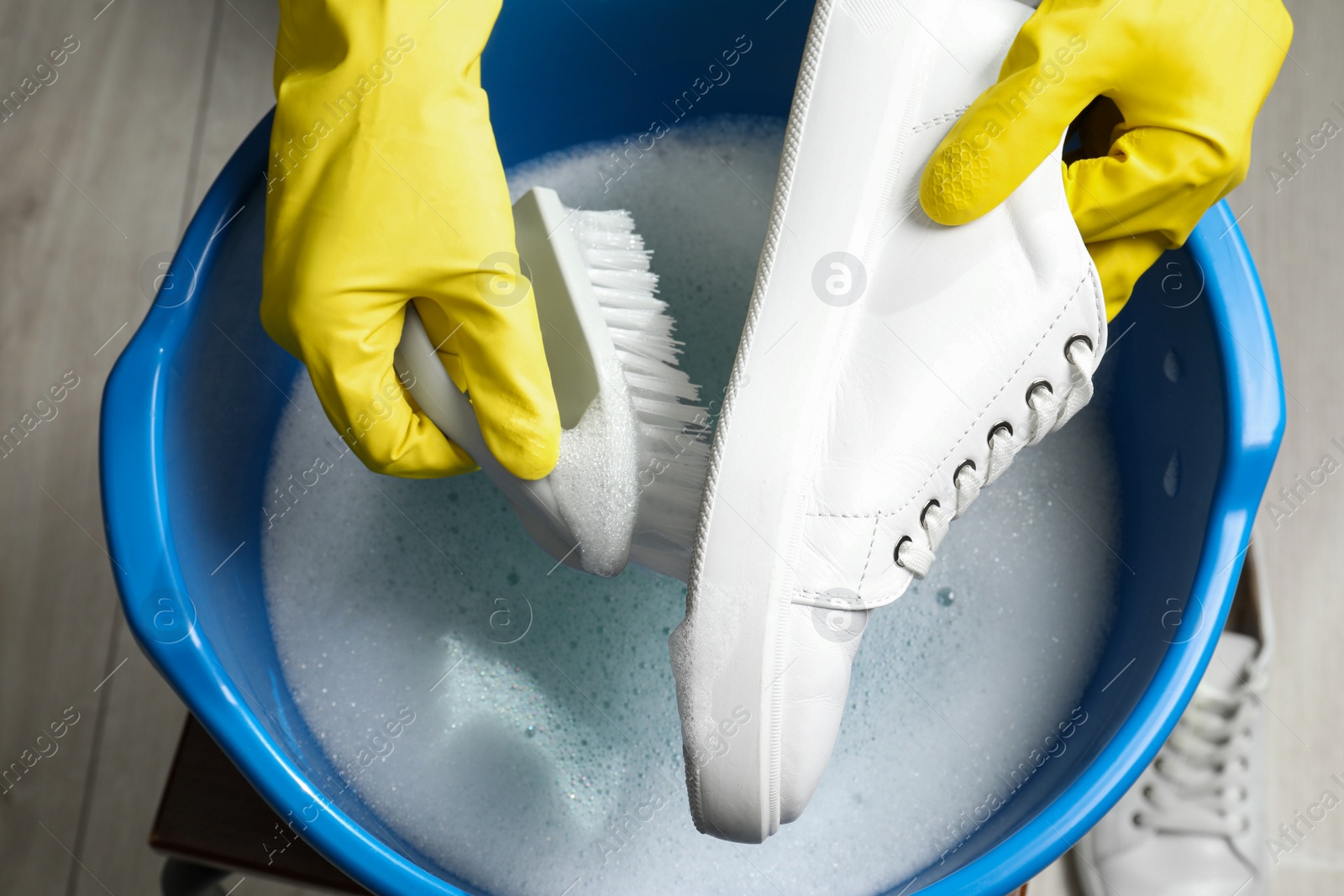 Photo of Woman with gloves and brush cleaning stylish sneakers in wash basin, top view