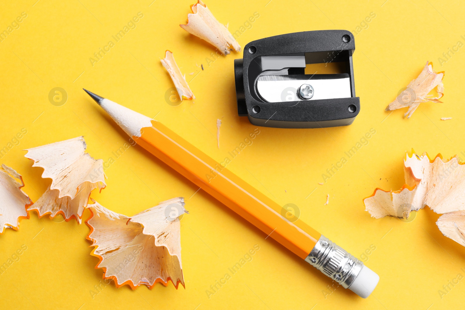 Photo of Pencil, sharpener and shavings on yellow background, flat lay