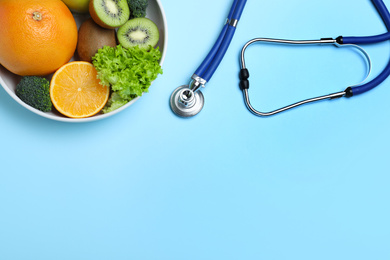 Photo of Fruits, vegetables and stethoscope on light blue background, flat lay with space for text. Visiting nutritionist